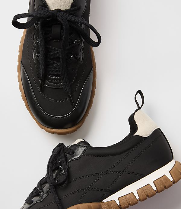 Black sneakers with tan soles are laid out on a white background.