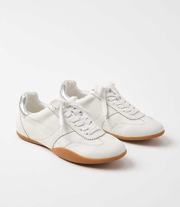 A pair of white leather sneakers with gum soles and silver accents rests on a plain white background.
