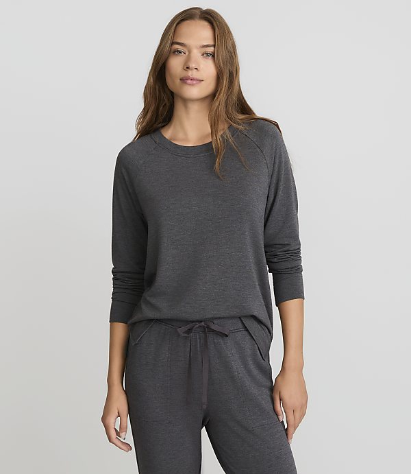 A woman in a dark grey long-sleeved shirt and matching pants stands against a plain grey background.