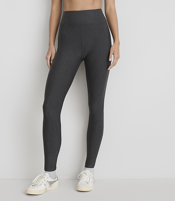 A person wearing dark grey ribbed leggings and white sneakers stands against a plain white background.