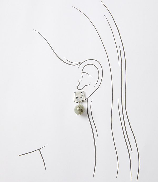 A square-shaped earring with a speckled pattern hangs from a stylized ear, set against a simple white background.