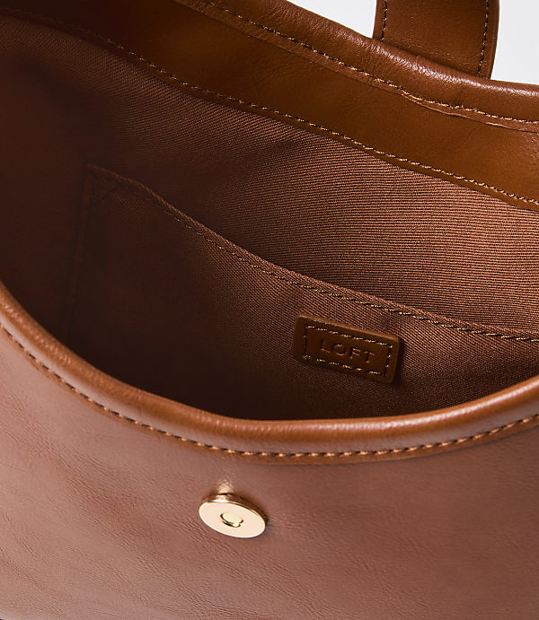 A close-up view of the interior of a brown leather handbag with a small pocket and a gold snap closure is visible against a plain background.