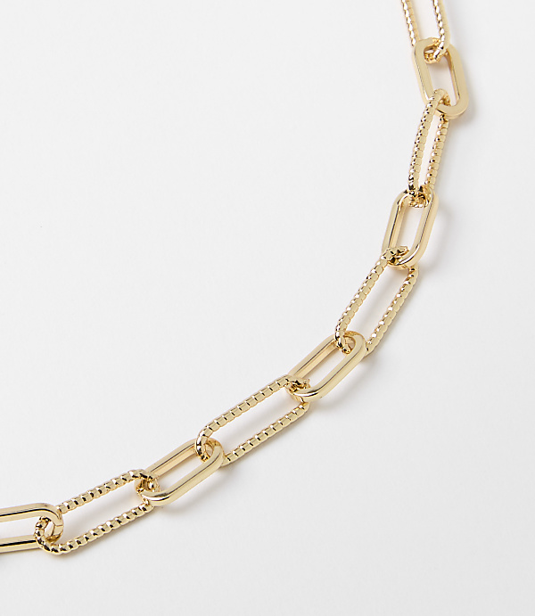 A gold paperclip chain necklace with textured links lies on a plain white background.