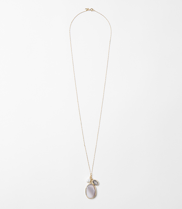 A delicate rose gold chain necklace with a pearlescent oval pendant and a small grey stone hangs against a plain white background.