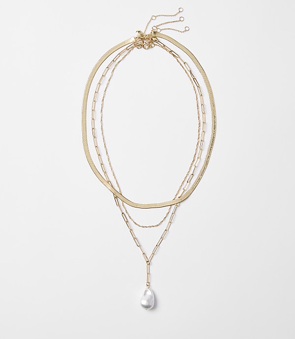 Three delicate gold necklaces, one with a single baroque pearl pendant, are arranged against a plain white background.