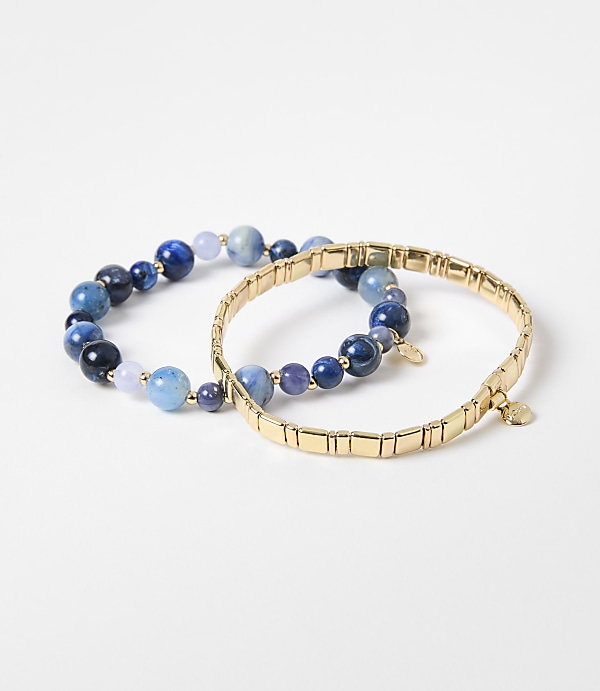 Two bracelets, one with blue beads and the other a gold chain, rest on a plain white background.
