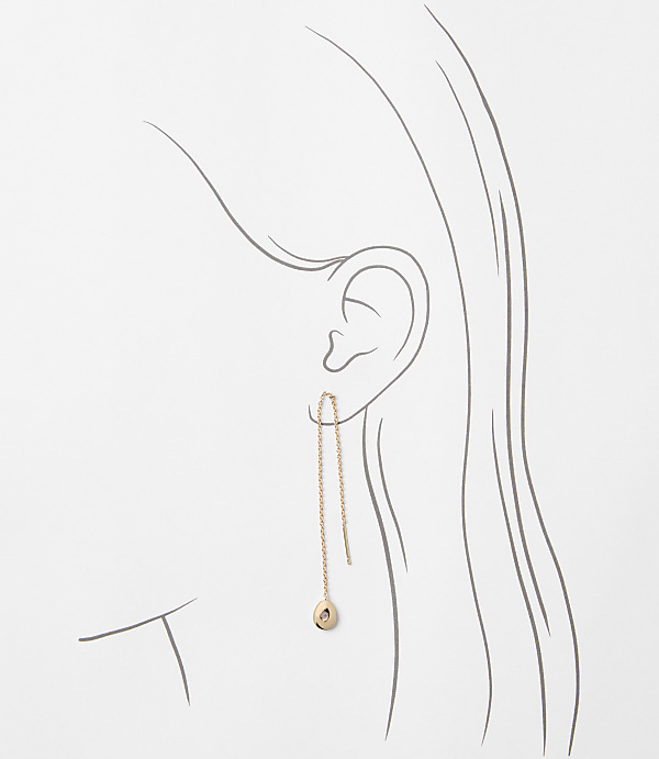 A delicate rose gold threader earring with a small charm dangles from an ear, set against a minimalist line drawing of a woman's head and neck.