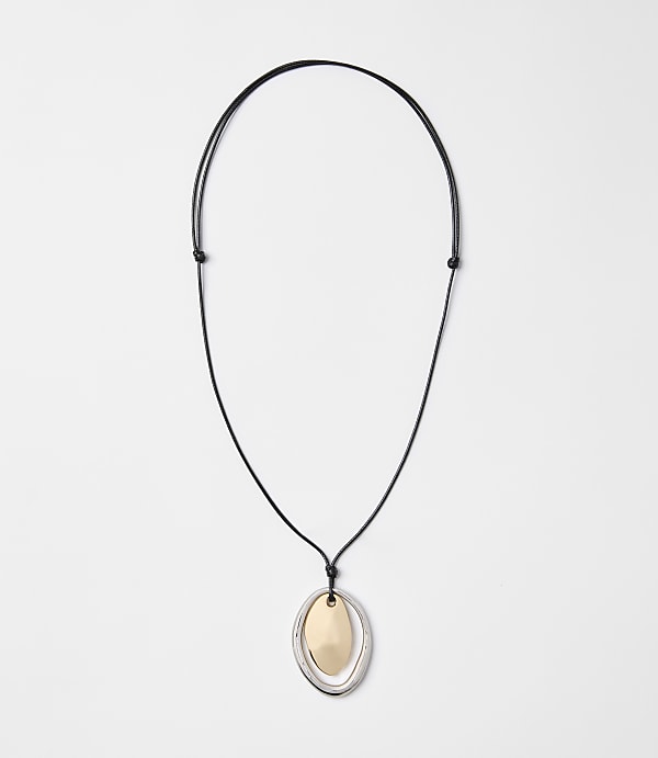 A black cord necklace with a layered oval pendant of gold and silver hangs against a plain white background.