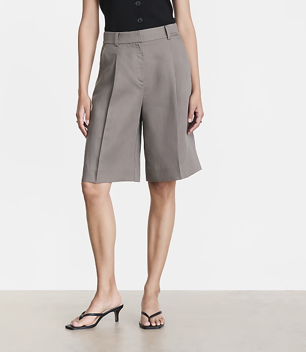 A woman stands in grey culottes and black heeled sandals against a plain white background.