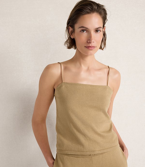 A woman in a tan camisole stands against a textured, light-colored background.