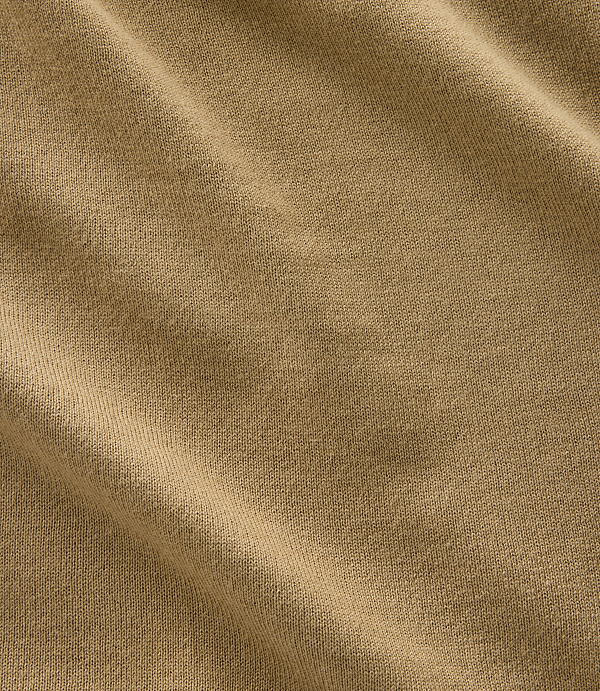 A close-up of tan fabric with soft folds and a textured weave fills the frame.