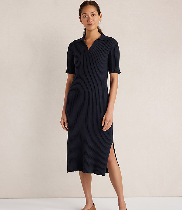 A woman in a navy blue ribbed knit polo dress stands against a plain, light-colored background.
