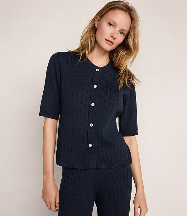 A woman in a navy ribbed cardigan and matching pants stands against a plain, light-colored background.