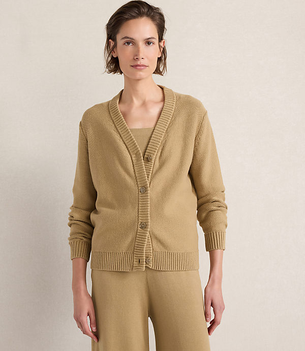 A woman in a tan cardigan and matching pants stands against a plain, light-colored background.