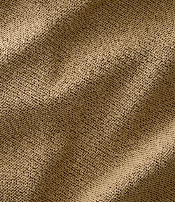 A close-up view of a textured, tan knitted fabric fills the frame, with soft folds and shadows creating depth.