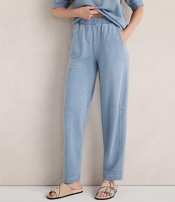 A person stands in light blue loungewear and sandals against a textured, light-colored wall.