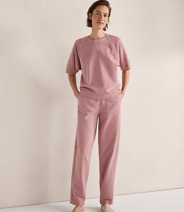 A woman in a pink loungewear set stands against a plain, textured background.