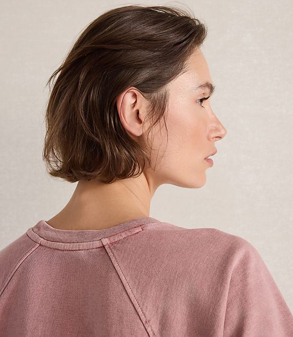 A woman with short brown hair in a pink sweatshirt is shown in profile against a textured, light-colored background.