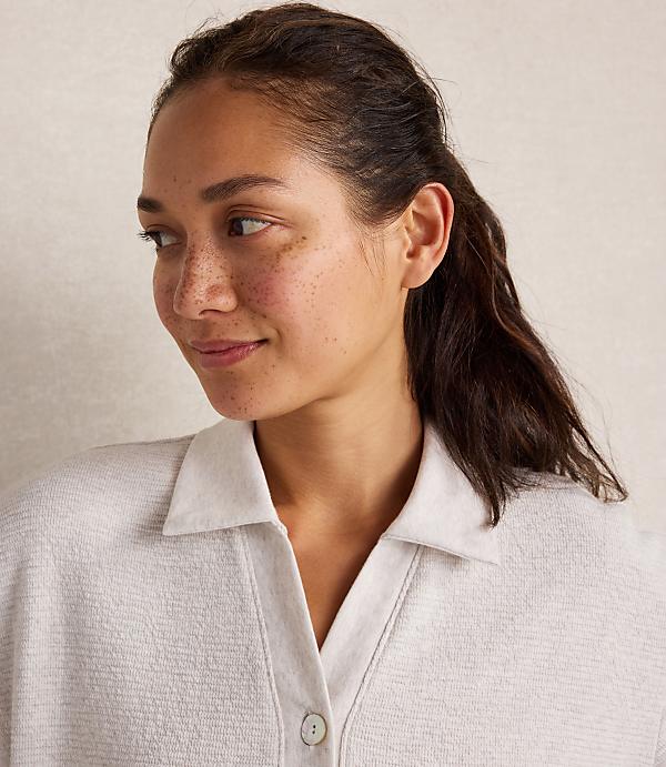 A woman with freckles and her hair in a ponytail smiles softly in the foreground, against a plain, light-colored background.