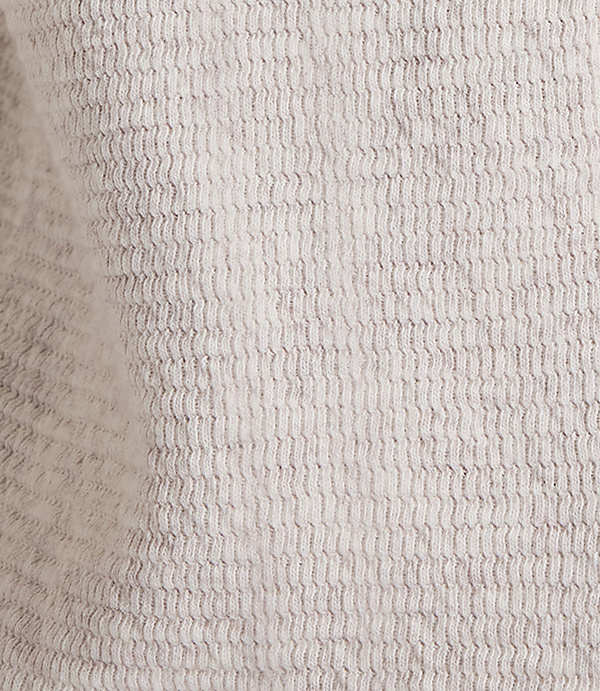 A close-up of a textured, light gray fabric with a subtle wave pattern fills the frame, with soft shadows and highlights creating depth.