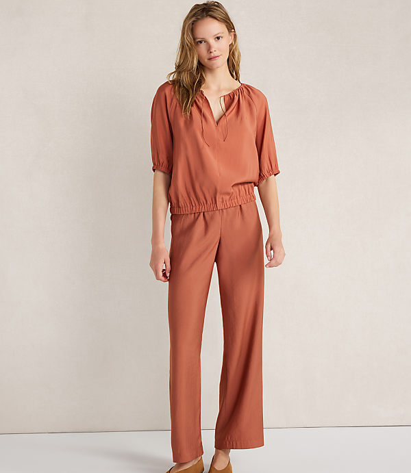 A woman in a rust-colored jumpsuit stands against a plain white background.