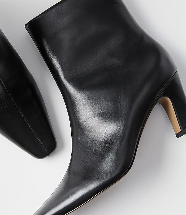 A pair of sleek black leather ankle boots with pointed toes and block heels rests on a plain white background.