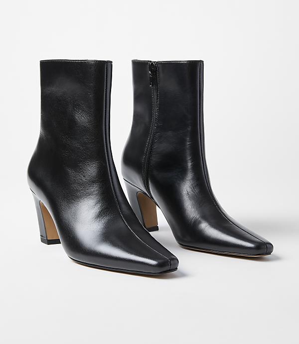 A pair of black leather ankle boots with square toes and block heels stand on a white background.