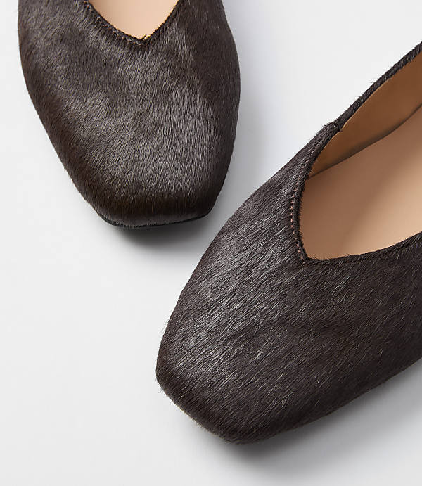 Two dark brown, furry flats with square toes are in the foreground against a plain white background.