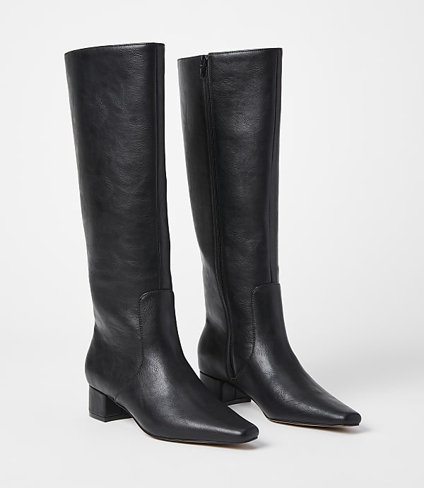 A pair of black leather knee-high boots with a low block heel stand on a white background.