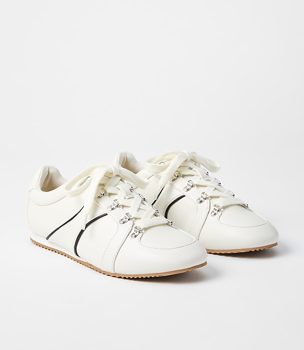 A pair of white leather sneakers with crystal embellishments and black accents are displayed against a plain white background.