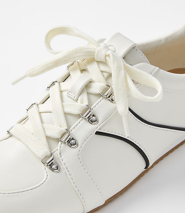 A white sneaker with cream laces is shown in close-up against a plain white background.