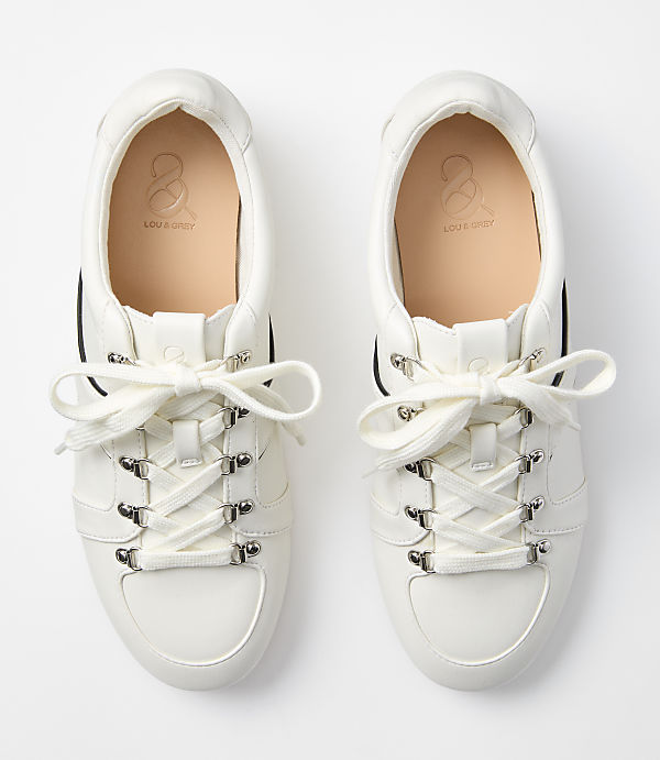 A pair of white leather sneakers with cream laces are laid out on a plain white background.