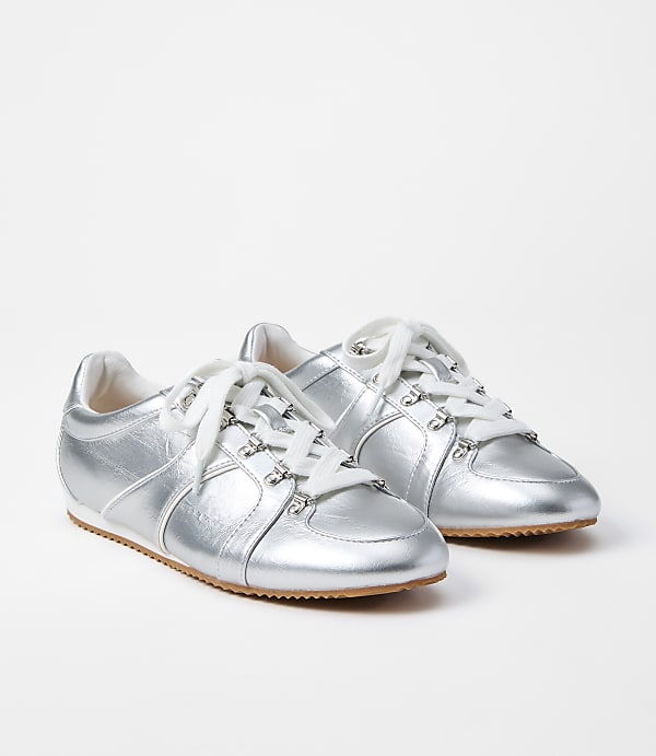 A pair of shiny silver sneakers with white laces rests on a plain white background.