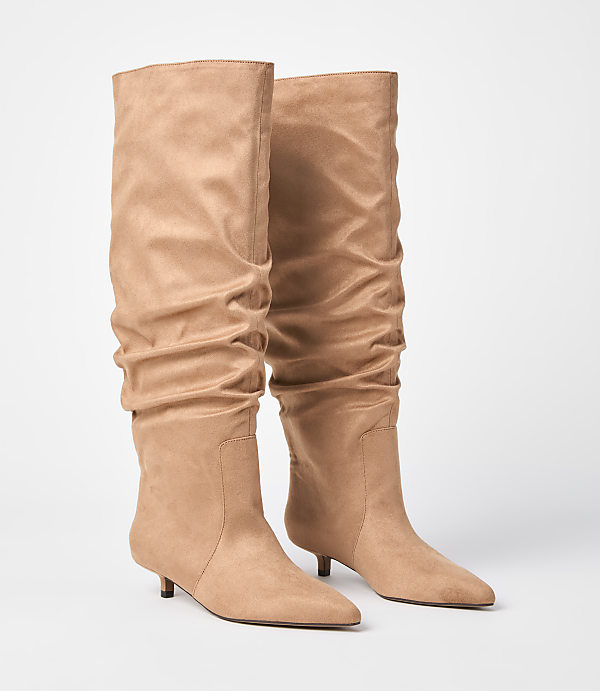 A pair of tan slouch boots with kitten heels stand on a white background.