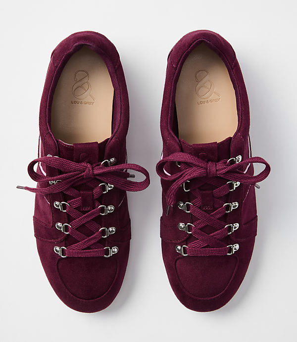 A pair of burgundy suede sneakers with silver eyelets and laces are laid out on a white background.