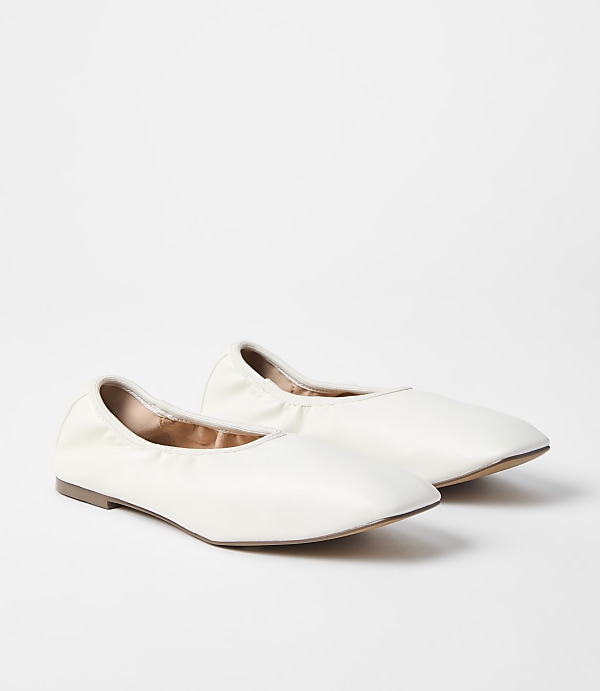 A pair of white ballet flats rests on a plain white background.