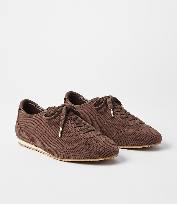 A pair of brown corduroy sneakers with gold-tipped laces rests on a plain white background.