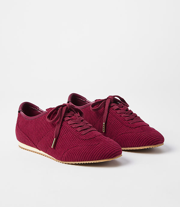 A pair of burgundy corduroy sneakers with white soles rests on a plain white background.