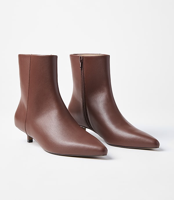 A pair of brown leather ankle boots with pointed toes and kitten heels are displayed against a plain white background.