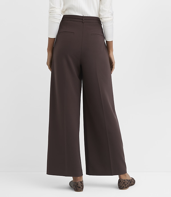 A person wearing brown wide-leg pants and leopard print flats stands against a plain white background.