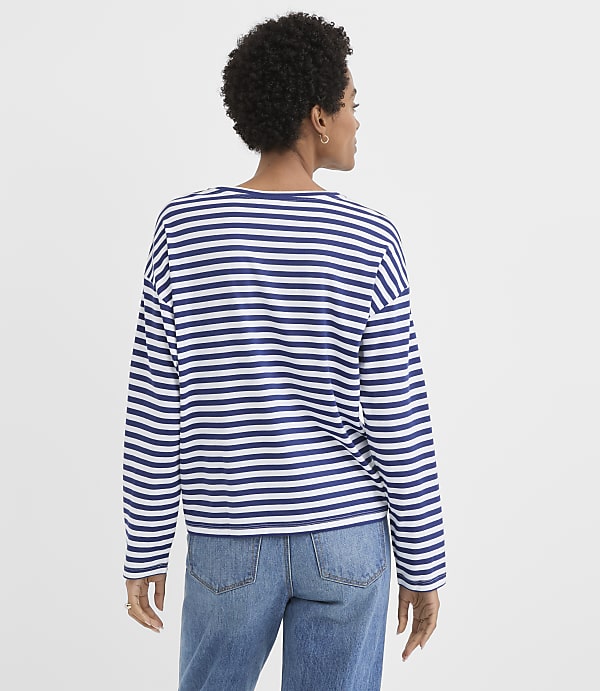 A woman in a striped shirt and jeans stands against a plain white background.