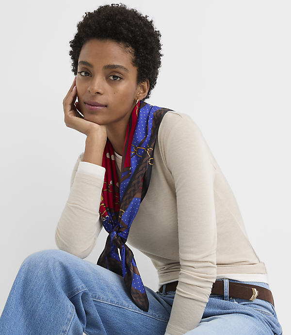 A woman with short, dark, curly hair and a patterned scarf tied around her neck poses against a plain white background.