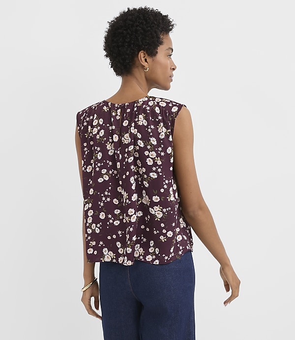 A woman in a floral top and jeans stands against a plain white background.