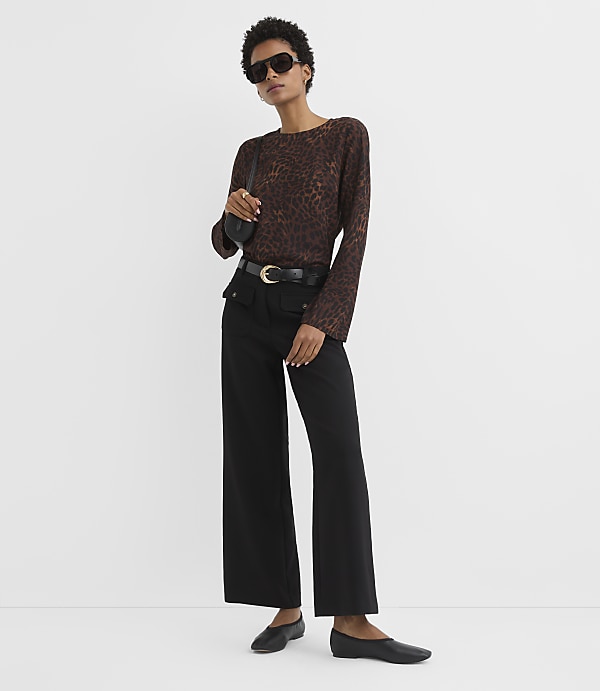 A woman in a leopard print top and black pants stands against a plain white background.