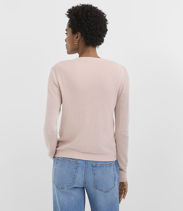 A woman in a pink sweater and blue jeans stands against a plain white background.