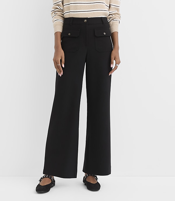 A person wearing black wide-leg pants with buttoned pockets and a striped sweater stands against a plain white background.