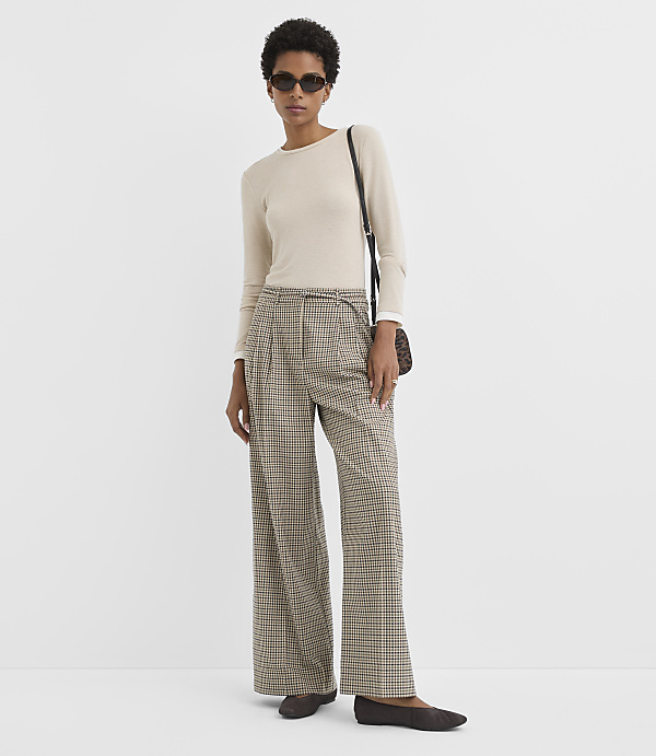 A woman in a cream-colored long-sleeved shirt and plaid wide-leg pants stands against a plain white background.
