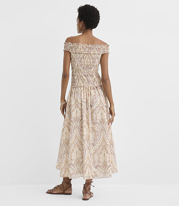 A woman in a patterned off-the-shoulder dress stands against a plain white background.