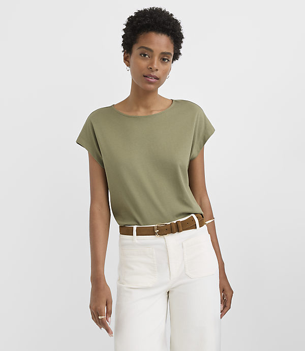 A woman in a green t-shirt and white pants stands against a plain gray background.