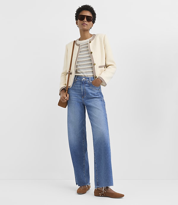 A woman in a cream jacket and striped shirt stands against a plain white background.